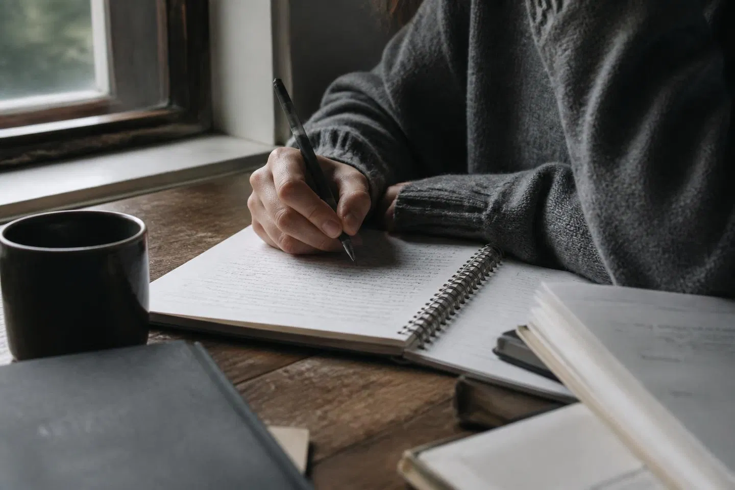 A student's hands writing in a notebook beside a window